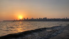 the sun is setting over an ocean with waves in front of it and a city skyline