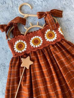 an orange and white dress with sunflowers is hanging on a wooden hanger