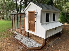 a chicken coop in the middle of a field with gravel around it and a wooden door