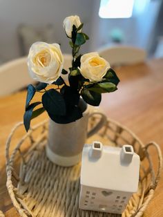 white roses in a vase sitting on a wicker tray next to a nintendo wii controller