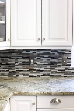 a kitchen with white cabinets and marble counter tops