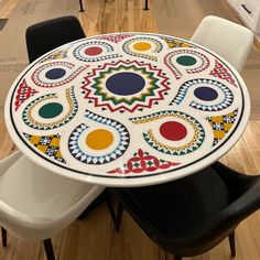 a white table with colorful designs on it and black chairs in front of the table