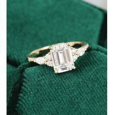 an emerald colored diamond ring sitting on top of a green cloth