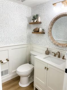 a white toilet sitting next to a sink in a bathroom under a large round mirror