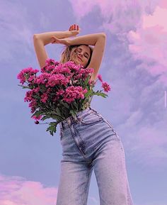 a woman is holding flowers in her jeans and posing for the camera with her hands behind her head