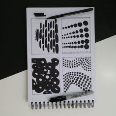 an open notebook with black and white designs on it, next to a marker pen