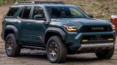 the front end of a green toyota pickup truck parked on a dirt road next to a fire hydrant