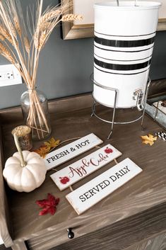 three wooden signs sitting on top of a table next to a white vase and pumpkin