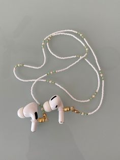 two ear buds are attached to a white beaded necklace on a gray surface with gold accents