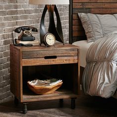 a bed with a wooden night stand next to a brick wall