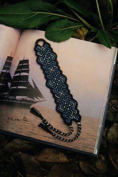 an open book with a black and blue braid on it next to a leafy plant