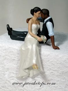 a bride and groom figurine sitting on top of a white tablecloth covered cake