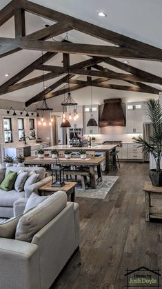 a large open concept kitchen and living room with wood flooring, exposed beams, white walls, and wooden floors