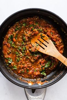 a wooden spoon in a skillet filled with food