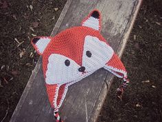 a crocheted hat with a red and white fox design on the front, sitting on top of a piece of wood