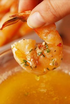 a person holding up a piece of shrimp over a bowl of broccoli soup