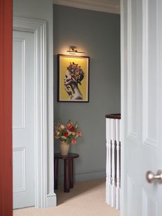 a painting hangs on the wall next to a table with flowers in front of it