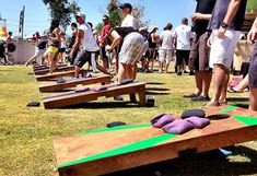 a group of people standing around wooden boards on the grass with purple pillows laying on them