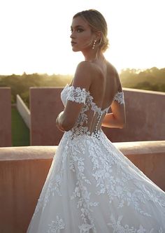 a woman in a white wedding dress standing on a balcony looking at the sun behind her