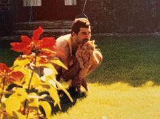 a man kneeling down in the grass with a frisbee near his face and flowers behind him