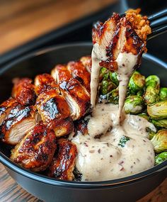 a bowl filled with chicken, brussel sprouts and sauce being drizzled over