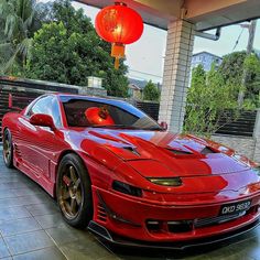 a red sports car parked in front of a building with lanterns hanging from it's roof