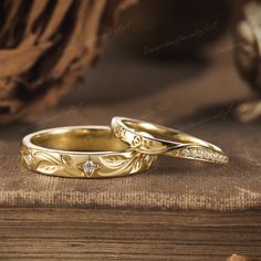 two gold wedding rings sitting on top of a wooden table