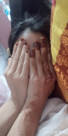 a woman laying in bed with her hands covering her face and eyes covered by henna