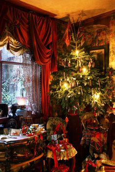 a christmas tree is lit up in the corner of a room with red drapes