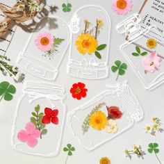 some flowers and leaves are in glass jars on a white table with other items around them