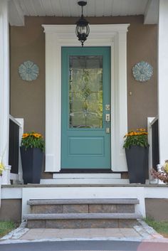 a blue front door with two planters on the steps and a light fixture above it