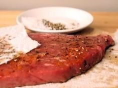 a piece of steak sitting on top of a table next to a bowl of seasoning