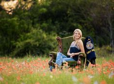 a woman sitting on a chair in the middle of a field with flowers and trees