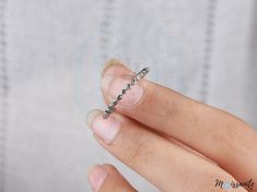 a woman's hand holding a silver ring with small beads on the middle of it