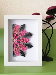 a pink and black flower in a white frame on a green table next to a lamp