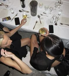 two women sitting at a table with wine glasses and silverware in their hands,