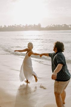 a man and woman holding hands on the beach