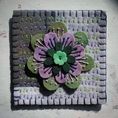 a flower made out of felt sitting on top of a piece of cloth with green and purple flowers