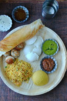 a wooden plate topped with different types of food next to sauces and condiments