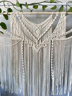 a white macrame hanging from a wooden pole next to a green plant with leaves on it