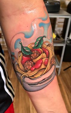 a person with a tattoo on their arm holding a plate of pasta and vegetables in it