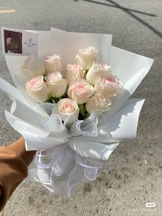 a bouquet of white and pink roses in someone's hand on the side of the road