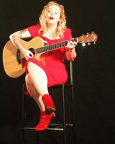 a woman sitting in a chair with a guitar on her lap and wearing red boots