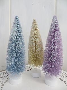 three small christmas trees sitting on top of a white doily covered table next to each other