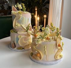 two decorated cakes sitting on top of a table next to each other with candles in the background