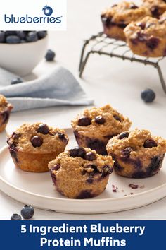 blueberry muffins on a white plate next to a bowl of blueberries