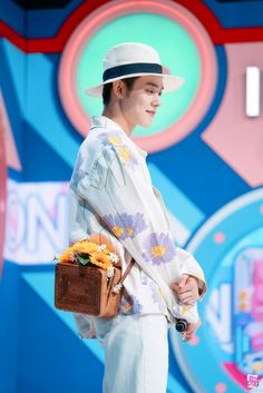 a male in a white shirt and hat is holding a brown basket with flowers on it