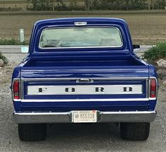 a blue pickup truck parked in a gravel parking lot next to a field and trees