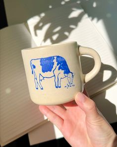 a hand holding a blue and white coffee cup with a cow design on the side