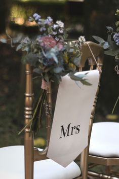 a chair with a sign and flowers on it sitting in front of some chairs outside